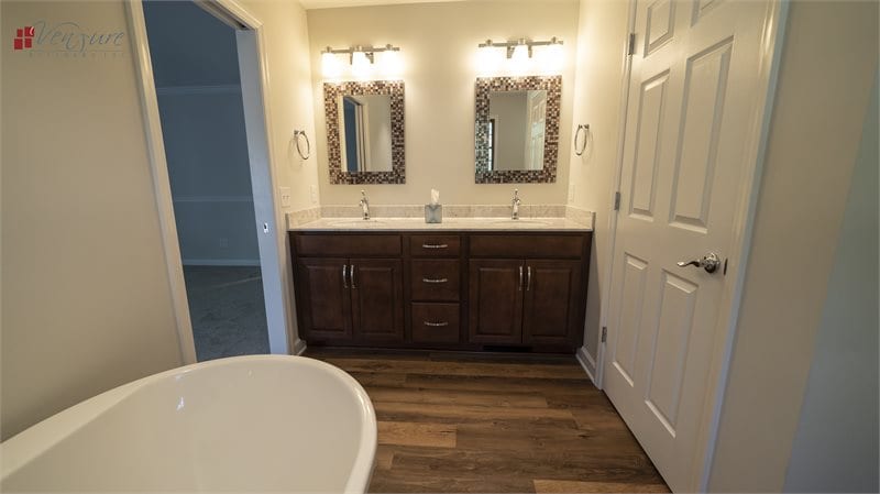 Bathroom with luxury vinyl planks, double bowl vanity, cultured marble vanity top, freestanding tub, chrome fixtures, two individual framed mirrors