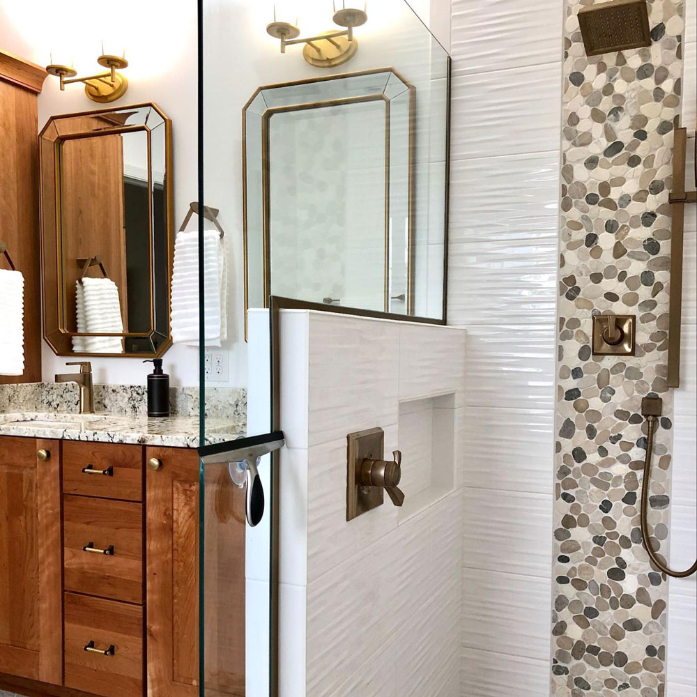 Shower with stone details next to double vanity with wood cabinets and granite countertop